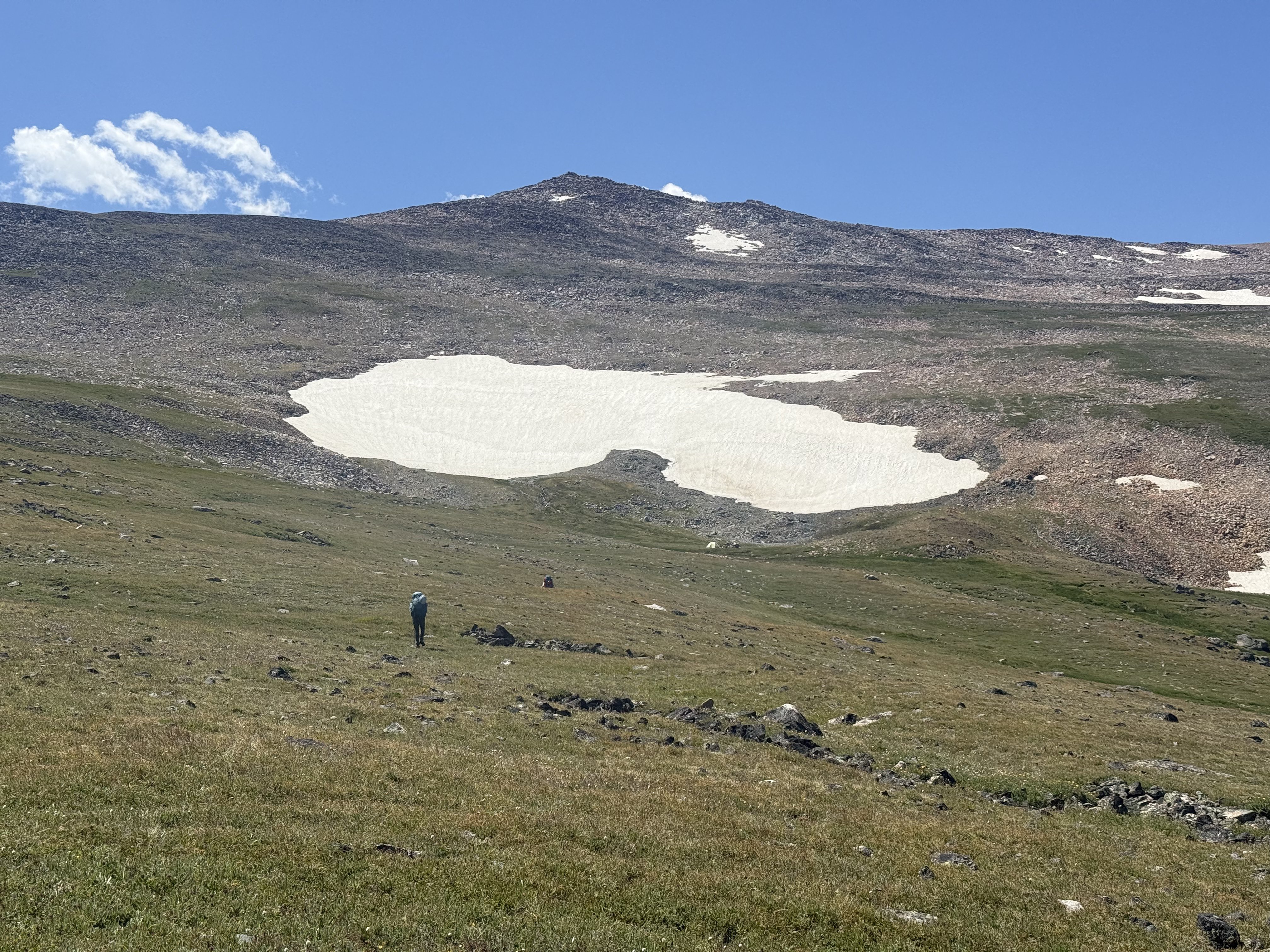 Hiker small against alpine snowfield and summit